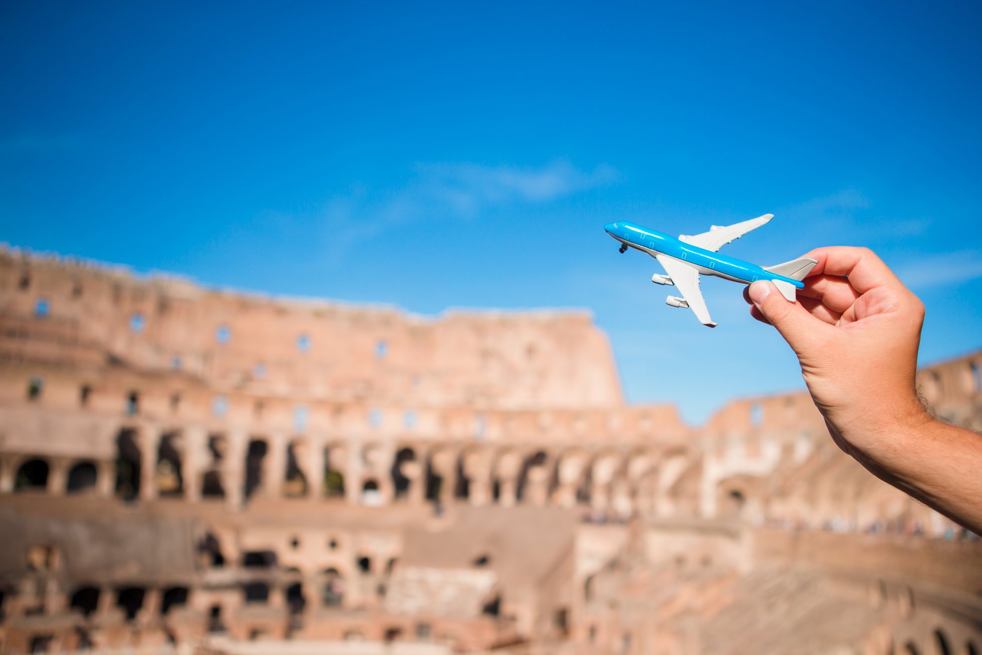 Hand Holding Toy Airplane Against Colosseum Background